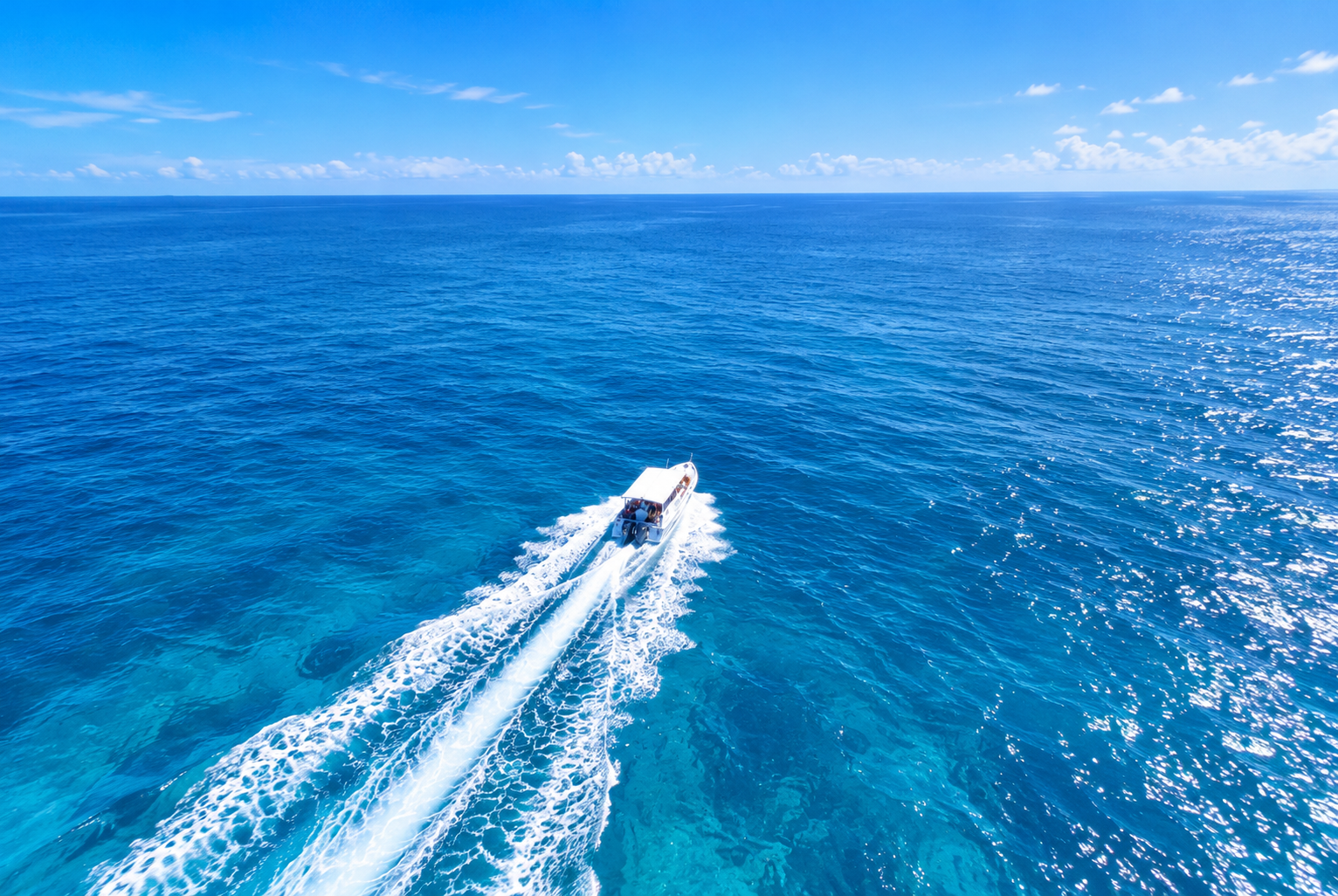 A speedboat seen from above crossing open blue water, leaving a white wake behind it